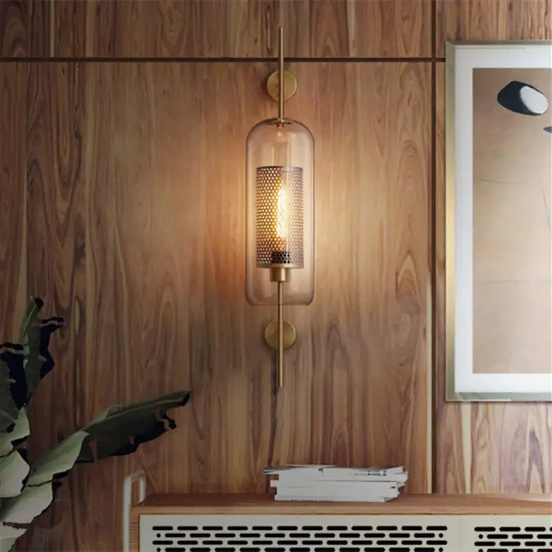 Brass-finished chiswick glass wall light sconce with clear glass cylinder and illuminated mesh-covered bulb for home décor