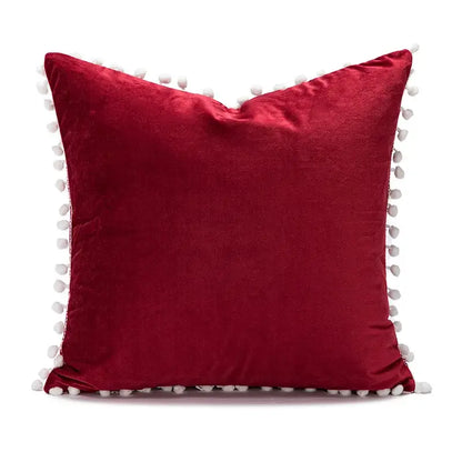 A plush red velvet decorbites christmas bow patchwork pillow cover with white pom-poms for festive home decor