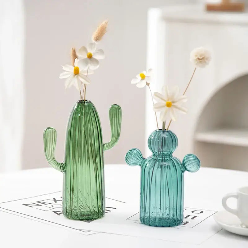 Two translucent colorful cactus glass vases in green and teal blue holding dried white daisies for home decor