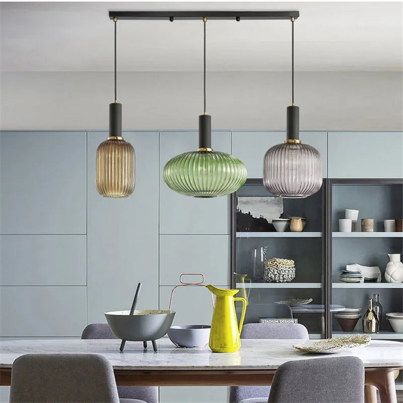 Three modern decorbites colorful glass pendant lights with ribbed amber green and grayish blue shades hang from black rods