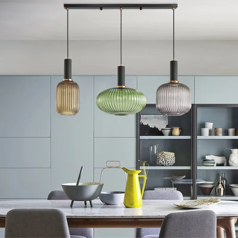 Three colorful glass pendant lights with amber green and gray ribbed shades hang above dining table by DecorBites