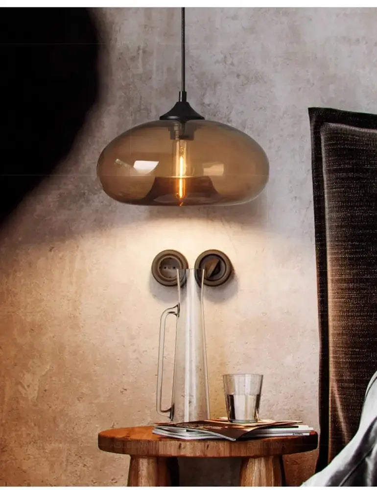 A warm amber glass colorful LED pendant light with black metal fixture hangs above a rustic wooden table