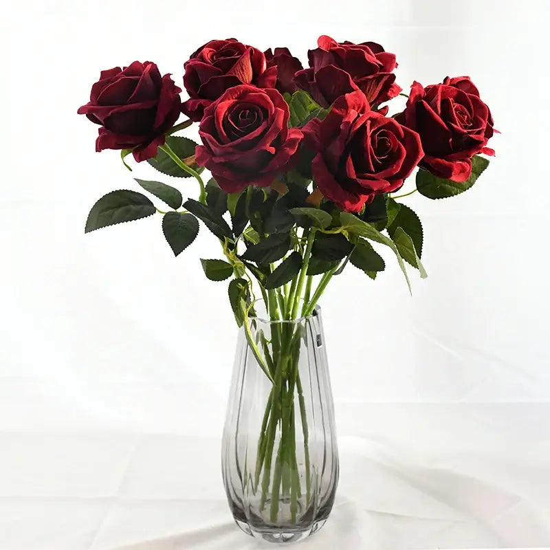 A clear ribbed glass flower vase holding deep red artificial roses for home décor by DecorBites™ colorful plastic flower
