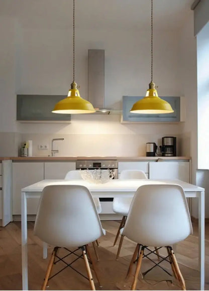 Two bright yellow colorful retro pendant lights with brass fixtures hang above a white dining table as pendant lights