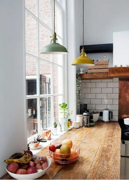 Two colorful retro pendant lights in sage green and mustard yellow hang from braided cords above a wooden counter