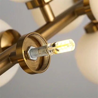 A warm glowing led bulb with clear glass and visible filament mounted in brass fixture of decorbites contemporary chandelier with white glass ball