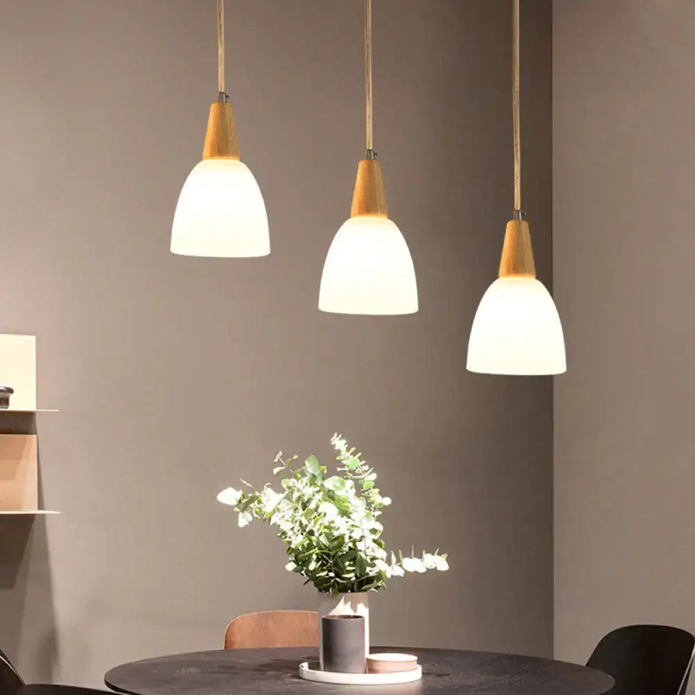 Three modern pendant lights with warm wooden tops and frosted glass dome shades in a minimalist dining space