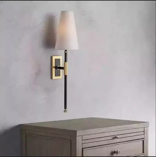 A sleek black and brass wall lamp with a copper cloth led tapered white fabric shade for bedroom use