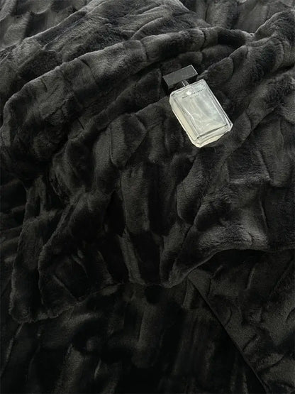 A sleek glass perfume bottle with a black cap resting on decorbites cozy faux rabbit fur bedding set in black and grey