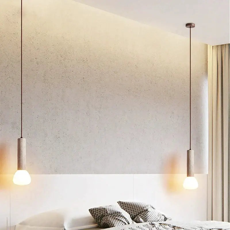 Two minimalist decorbites cream style pendant lamps with cylindrical concrete shades and warm glowing bulbs hanging