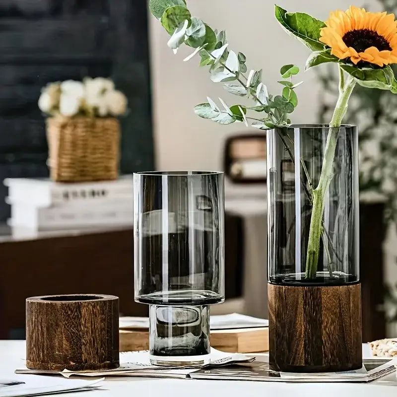 Tall translucent primary color glass vase with dark wood base holding sunflower and eucalyptus for living room decor