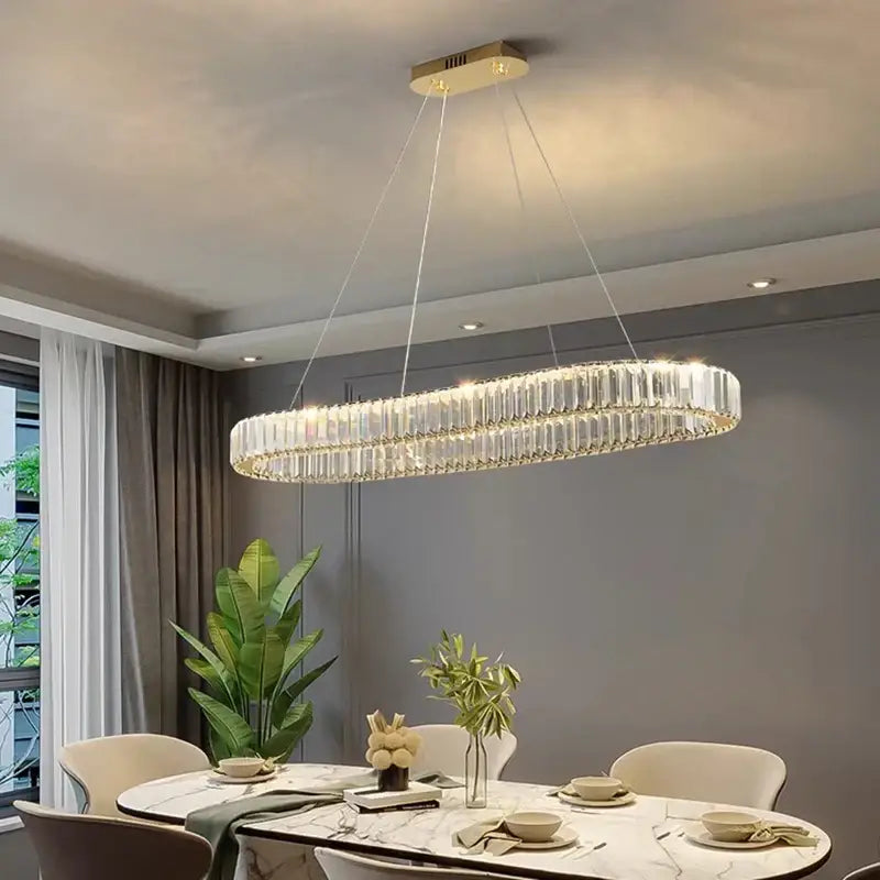 A modern oval-shaped decorbites crystal chandelier with gold-toned mount and wires for living and dining rooms