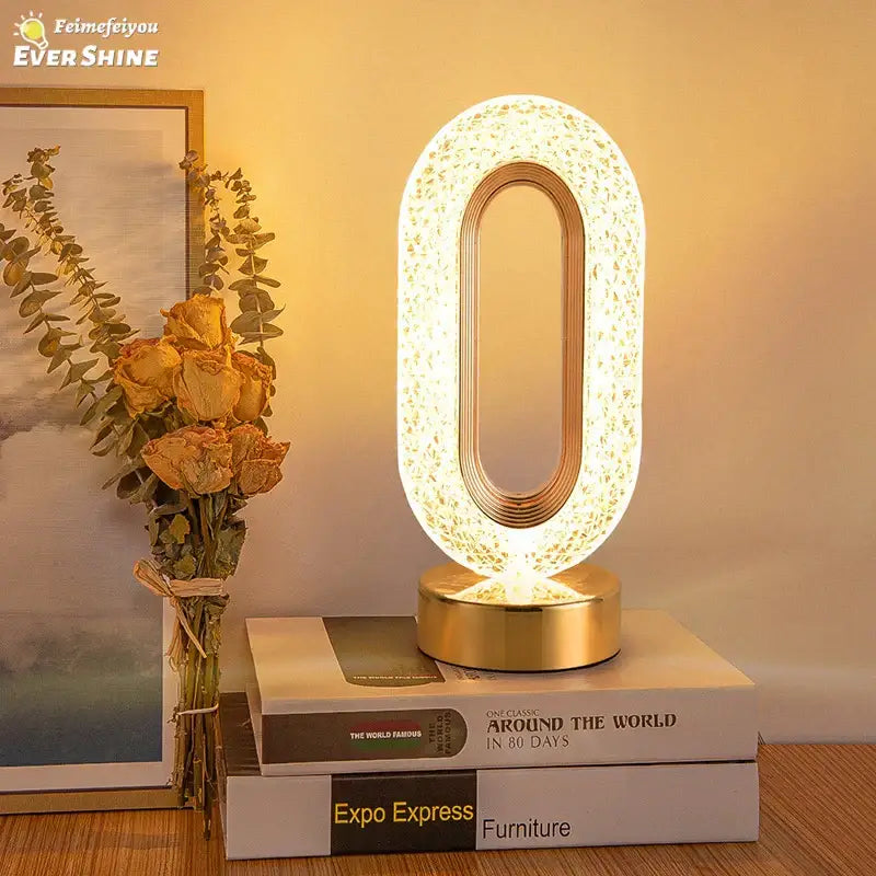 A glowing decorbites crystal led table lamp with an oval shape, gold-toned base, and illuminated crystal body for bedroom
