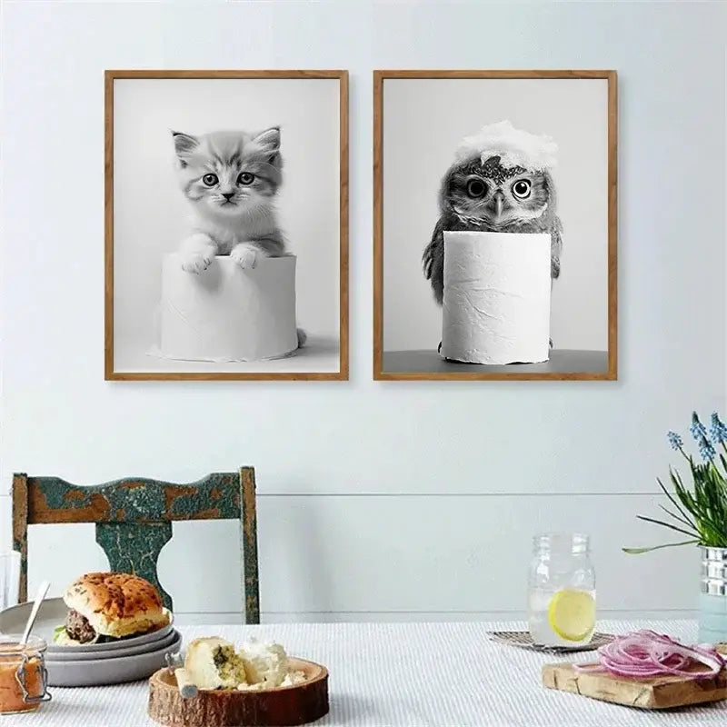 Two framed black and white cute animals canvas wall art featuring a kitten and owl peeking behind toilet paper rolls for bathroom decor