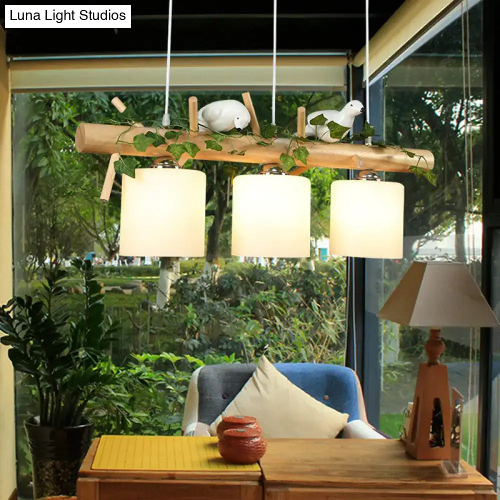 Natural wood branch pendant light with three cream cylindrical shades and white resin bird deco for country style restaurants