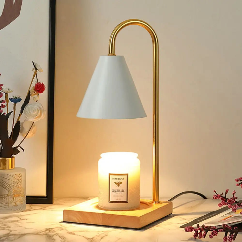 Gold-finished dimmable candle warmer lamp with white conical shade and wooden base illuminating a scented candle