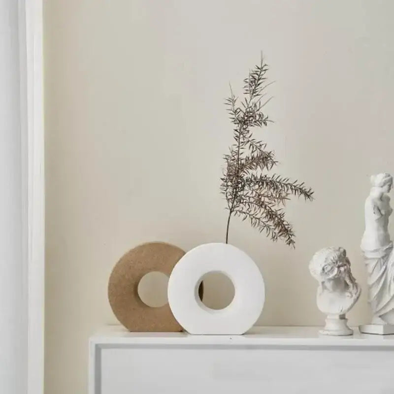 White ceramic donut vase with central hole beside tan circle and busts on white surface for home decor