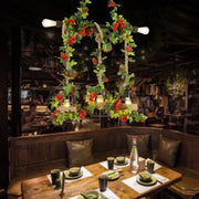 Rustic black metal island light pendant with five Edison bulbs, rope detail, and red roses draped over birdcages