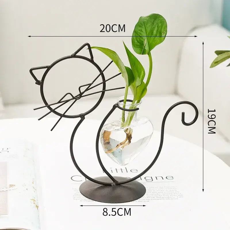 Black metal cat-shaped flamingo metal vase with clear glass heart container holding green plant stems for home decor