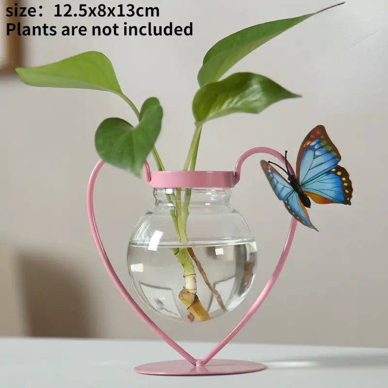 Pink heart-shaped flamingo metal vase holding a clear glass spherical vase with green stems for home decor