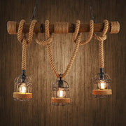 Rustic industrial ceiling light with three cast iron birdcage bulbs hanging by hemp rope from a wooden beam