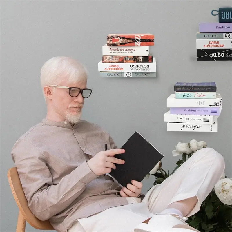A man in beige attire reads a book seated near DecorBites™ floating metal bookshelves 2pcs floating bookshelf set