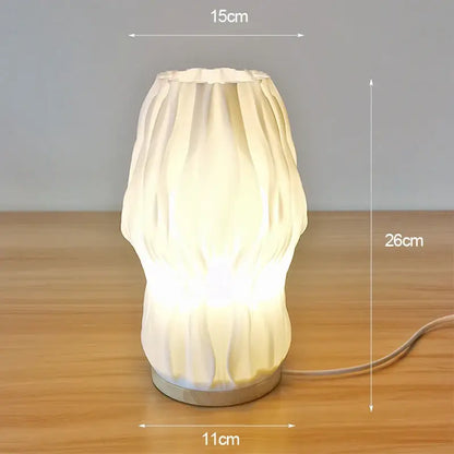 Cream-colored ribbed ceramic french cream style desk lamp with glowing base and metallic foot for bedside or study use