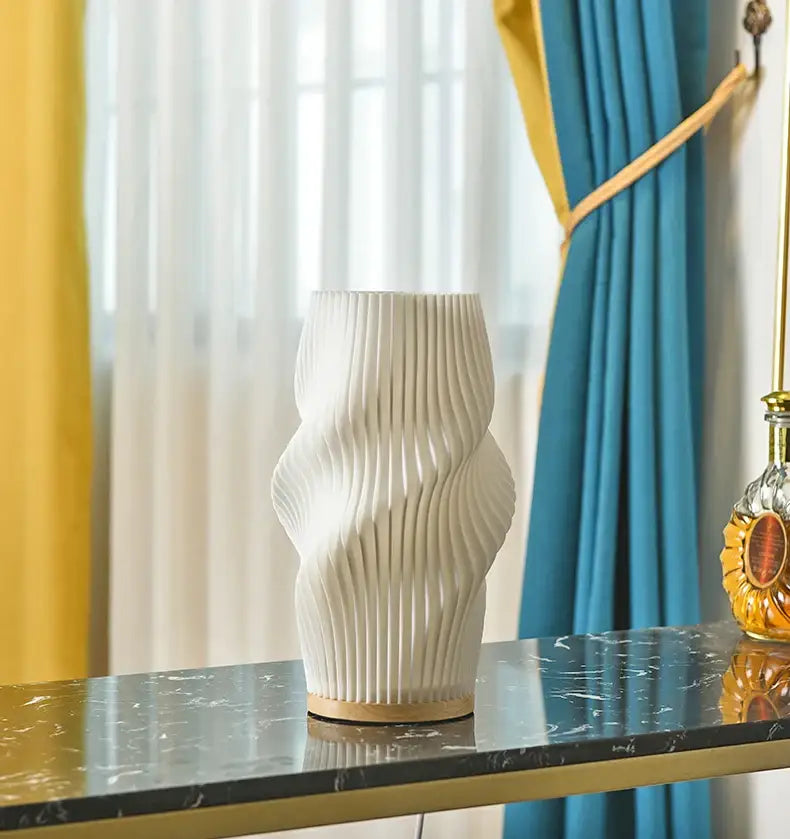 A white ceramic vase with wavy design on dark marble complements the french cream style desk lamp DecorBites™