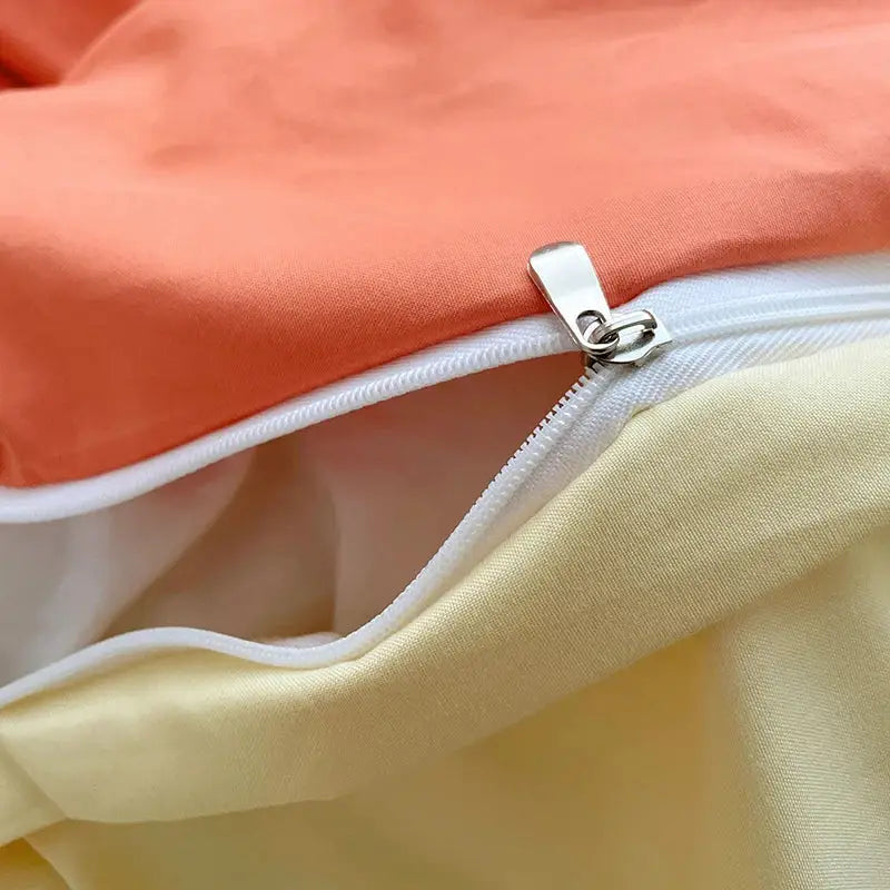 A close-up of a silver zipper with white stitching on the fresh solid color cotton quilt set fabric in peach and yellow