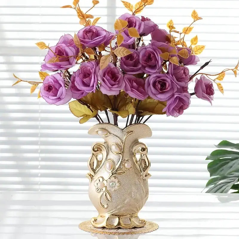 A gold-toned frosted porcelain flower vase with ornate floral embossing and artificial purple roses for home decor
