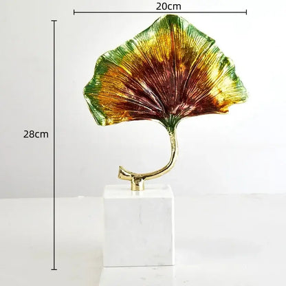 Vibrant iridescent decorbites ginkgo leaf metal sculpture with a golden stem on a white marble base for home decor