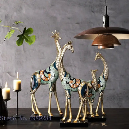 Three ornate decorbites giraffe mother and child painted sculptures with gold-toned legs and teal blue orange patterns on black bases