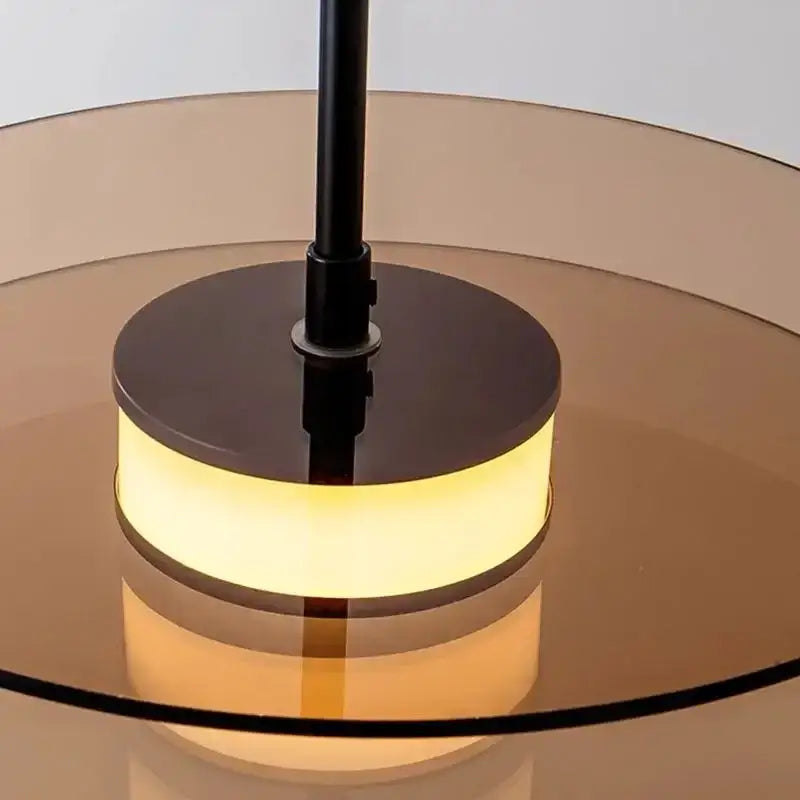 A DecorBites glass art chandelier featuring a sleek black stem and amber glass ring emitting warm LED light