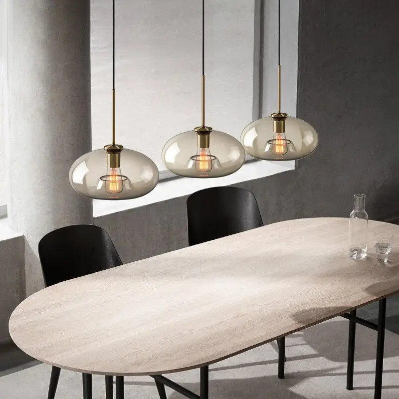 Three modern decorbites™ glass pendant lights with smoked glass globes and brass accents hanging above dining table