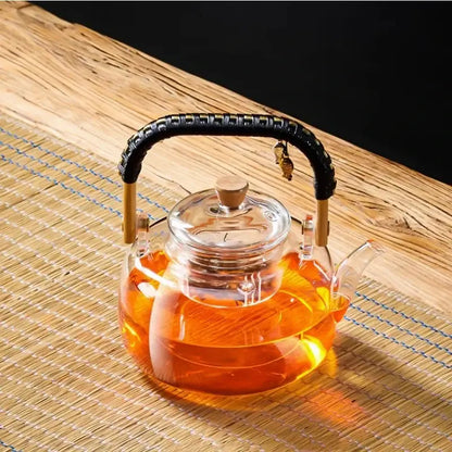 Clear glass decorbites glass tea pot with black weave handle wooden accents and amber tea inside