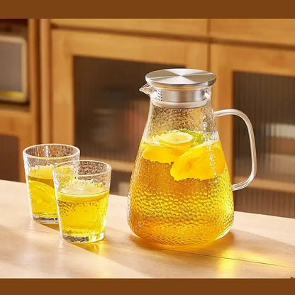 Clear hammered glass tea set pitcher with stainless steel silver lid and handle filled with lemon-infused liquid from decorbites
