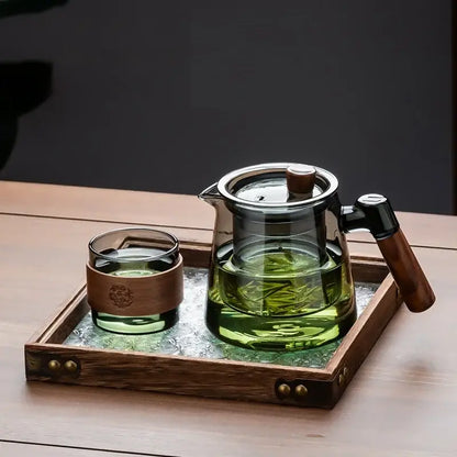 Clear glass teapot with wooden handle and lid filled with green tea on retro glass tray in DecorBites tea set