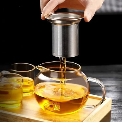 A stainless steel tea infuser straining golden tea into a decorbites glass teapot with kung fu style filter