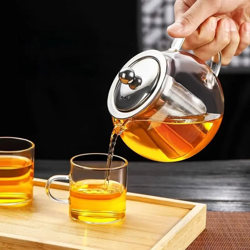 Decorbites glass teapot with stainless steel lid and built-in filter pouring amber tea into matching glass cups