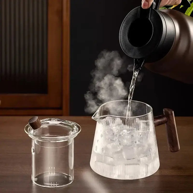 A decorbites glass teapot 900ml with wooden handle and lid being filled from a black thermal carafe for puer kung fu tea