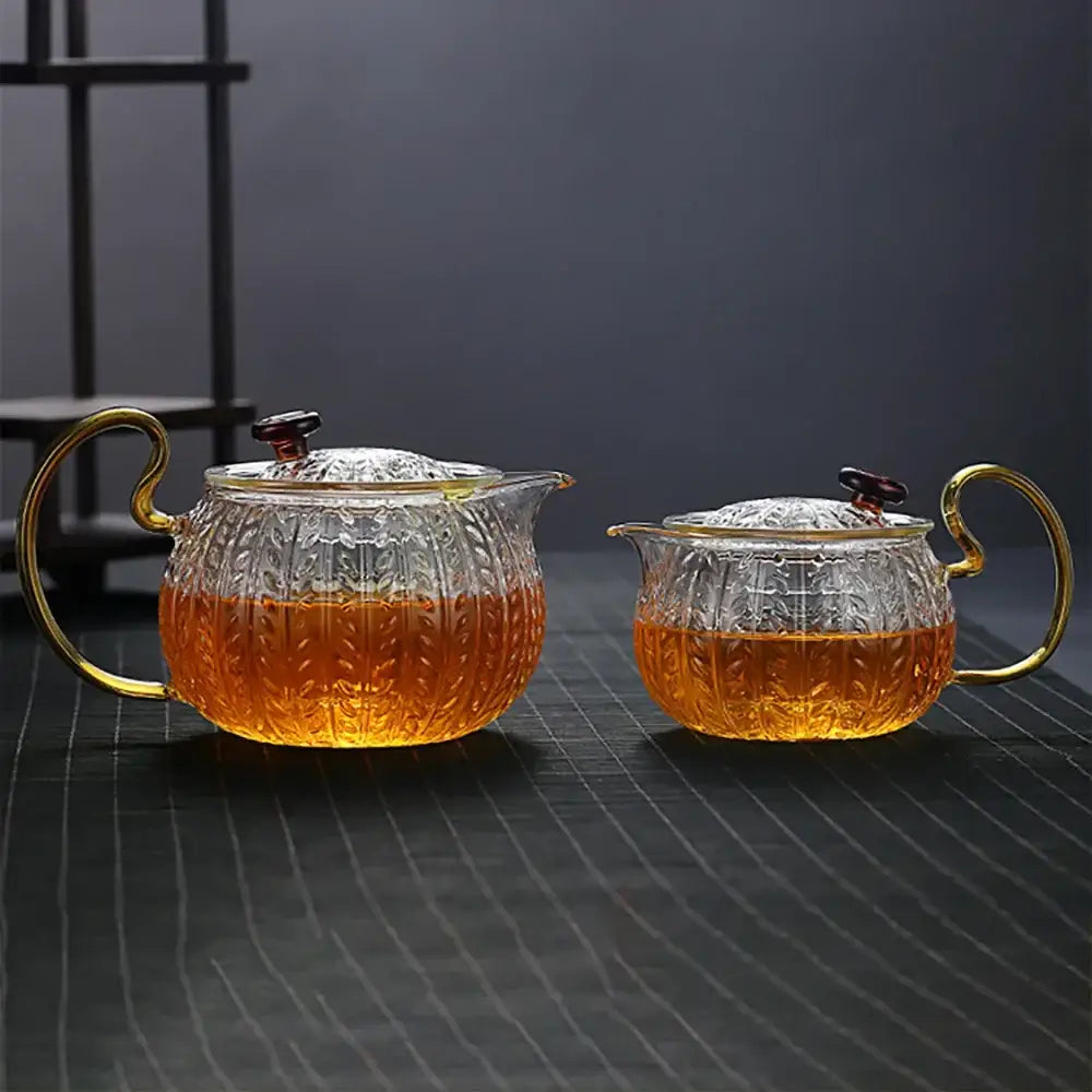 Set of two decorbites glass teapots with gold-toned handles and lids featuring etched leaf patterns for tea infusion