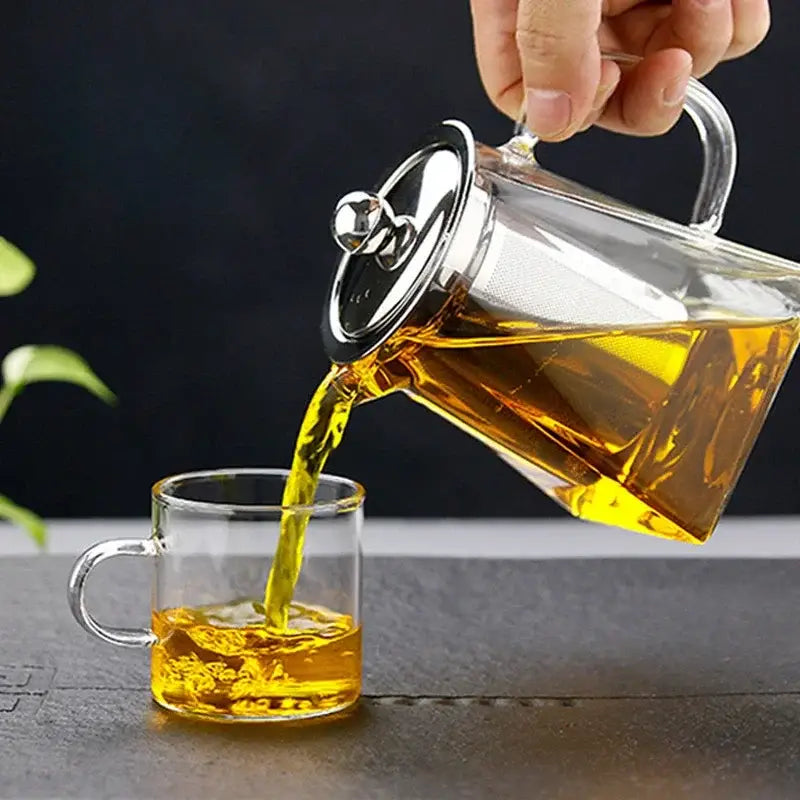 Decorbites glass teapot infuser with stainless steel lid pouring golden tea into matching clear glass mug for home use