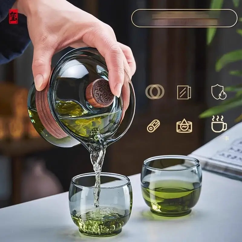 A clear glass teapot set with wooden lid and handle pouring green tea into matching cups from decorbites glass teapot