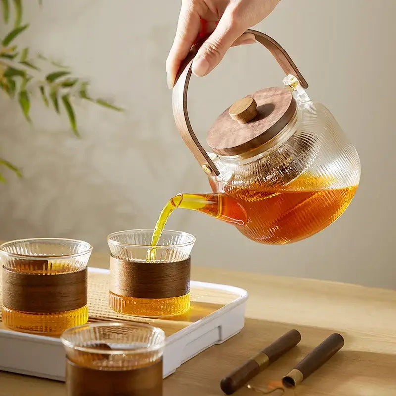 Clear glass teapot set with wooden handle and lid pouring amber tea by DecorBites glass teapot set