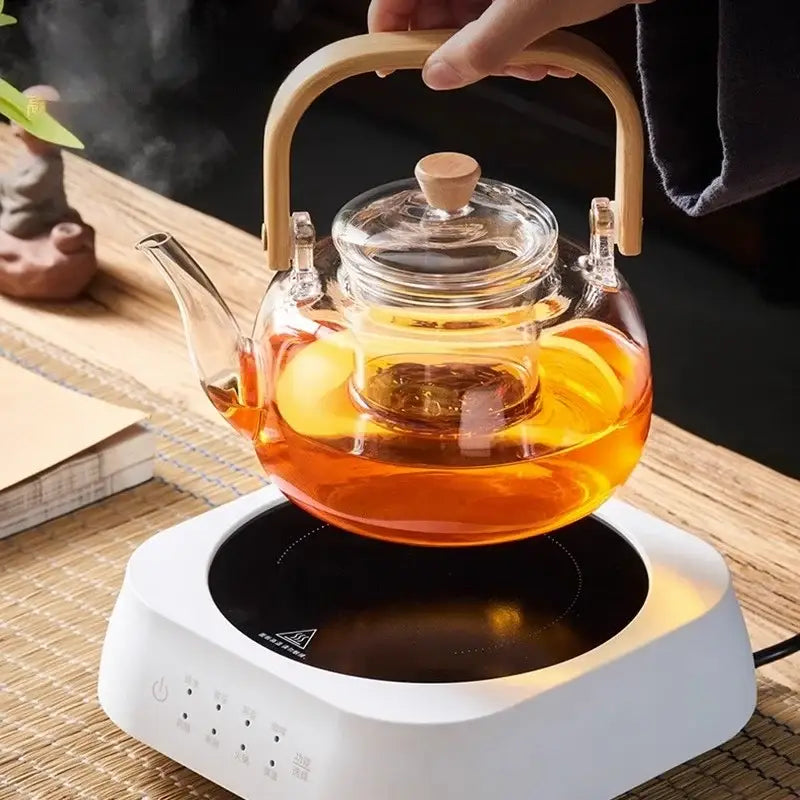 Clear glass teapot with wooden handle and lid knob filled with amber tea in decorbites glass teapot set
