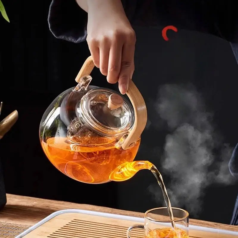 A decorbites glass teapot with wooden handle and lid knob filled with steaming orange tea for kung fu tea set