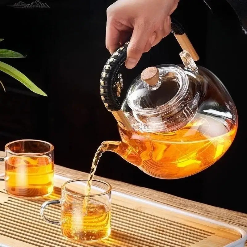 Clear glass teapot with wooden handle pouring amber tea into glasses from the DecorBites glass teapot set