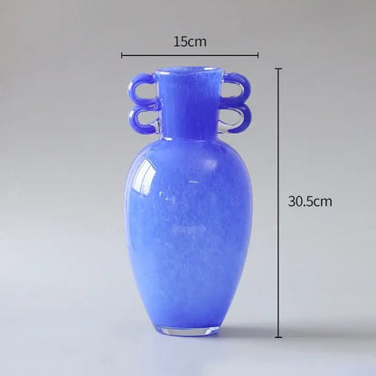 A decorbites glass vase in translucent cobalt blue with a rounded body narrow neck and ornate looped handles for decoration