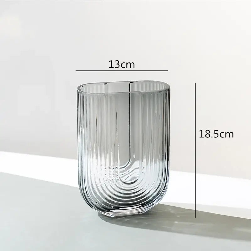 A sleek transparent decorbites glass vase with vertical ribbed texture and modern curved design for flower arrangement