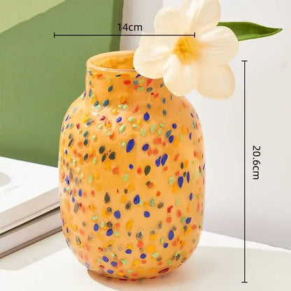 A vibrant orange DecorBites glass vase with colorful speckles and a white flower on its rim for home decor